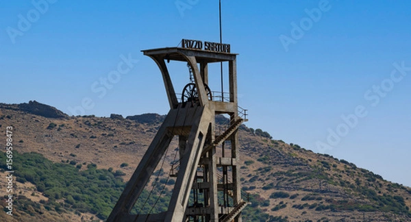Fototapeta Rusty industrial tower stands isolated against a dry hillside covered with sparse vegetation