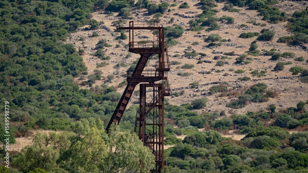 Fototapeta Rusty industrial tower stands isolated against a dry hillside covered with sparse vegetation