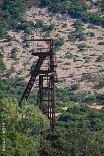 Fototapeta Rusty industrial tower stands isolated against a dry hillside covered with sparse vegetation