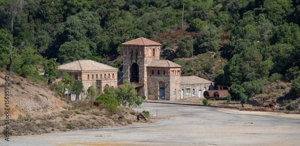 Fototapeta Rusty industrial tower stands isolated against a dry hillside covered with sparse vegetation