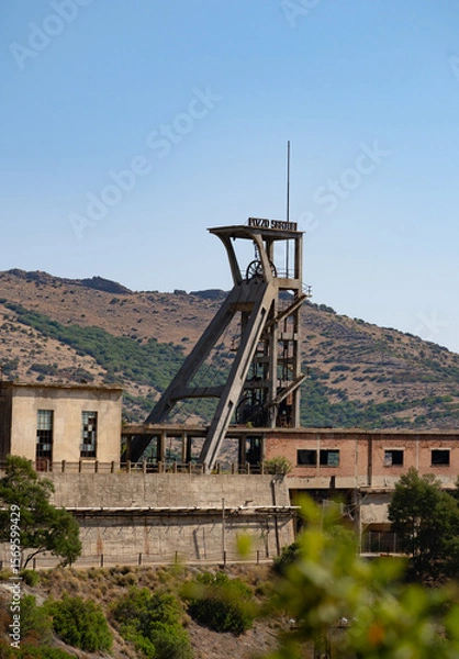 Fototapeta Rusty industrial tower stands isolated against a dry hillside covered with sparse vegetation