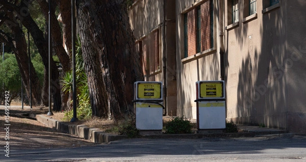Fototapeta Old gasoline and diesel pumps stand unused near a worn building and pine trees