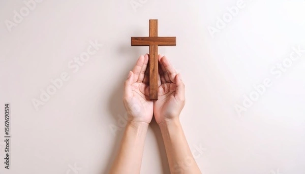 Fototapeta Faithful prayers, Wooden cross held in hands on a light background, symbolizes belief and spirituality