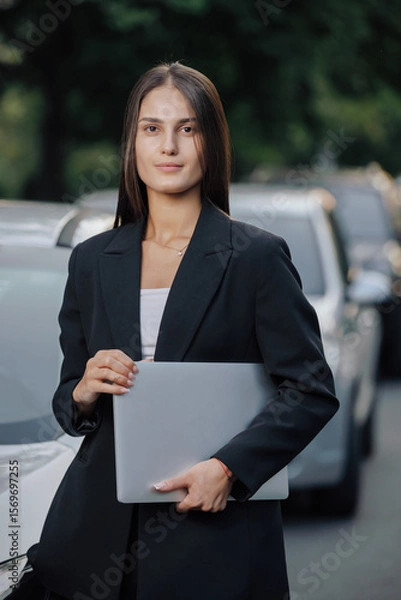 Obraz Woman in business suit stands with laptop near her car
