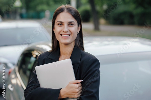 Obraz Woman in business suit holding laptop leaning on her car