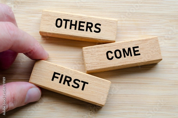 Fototapeta Others come first message on wood blocks, reinforcing the idea that effective leadership involves serving and uplifting others consistently