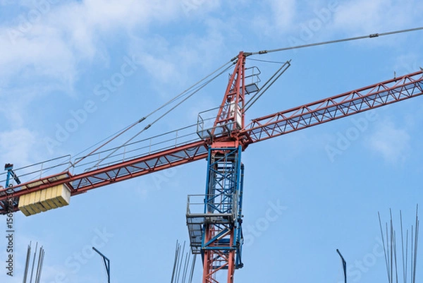 Obraz Red and blue tower crane at construction site. Detailed view of heavy machinery and urban steel structure.