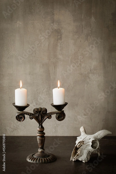 Fototapeta Beautiful vintage metal candelabrum with two burning candles and goats skull on the table, vertical image, copy space.