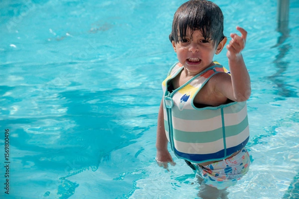 Fototapeta A young child is in a pool wearing a life jacket. The child is crying and pointing at something in the water