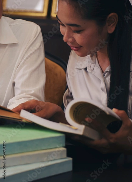 Fototapeta Two of Diversity Student study and reading book together in library at asian college. Happy multi ethnic woman search for knowledge in classroom at university. Education concept-vertical image.