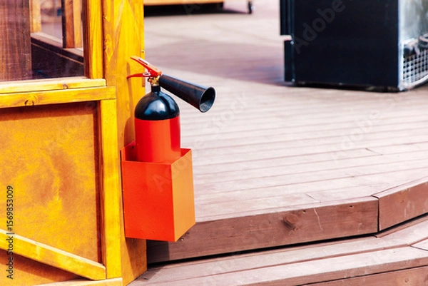 Obraz Fire extinguisher mounted on wooden structure near outdoor seating area