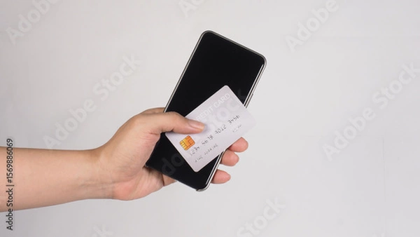 Fototapeta A hand holding a silver credit card and a smartphone ON white Background.