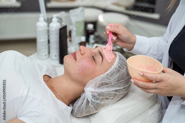 Fototapeta Young woman lying in spa and relax with with pink facial mask