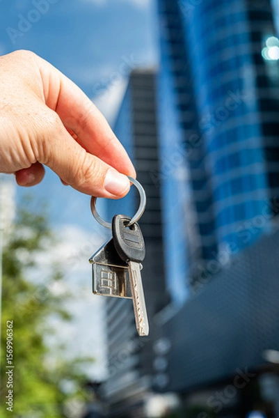 Fototapeta Keys to Success: Hand Holding Keys Against Futuristic Skyscraper. Symbolic image of a hand holding a bunch of keys with a modern glass skyscraper