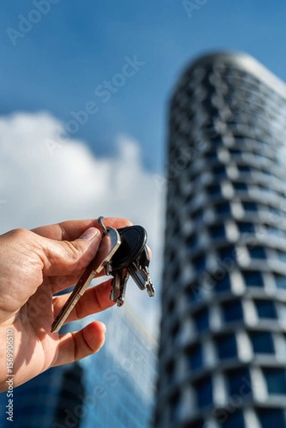 Fototapeta Keys to Success: Hand Holding Keys Against Futuristic Skyscraper. Symbolic image of a hand holding a bunch of keys with a modern glass skyscraper