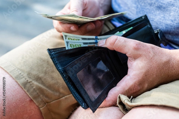 Fototapeta Man Holding US Dollar Bills in Wallet – Personal Finance and Cash Concept. Close-up of a man holding a black leather wallet filled with U.S. dollar bills.