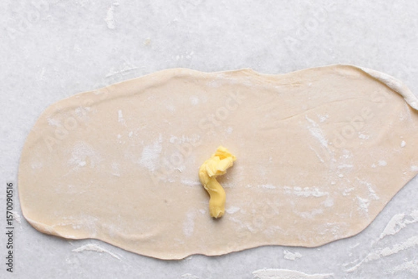 Obraz Overhead view of butter being spread on rolled out paratha dough, top view of flaky flatbread dough being covered with ghee, process of making paratha