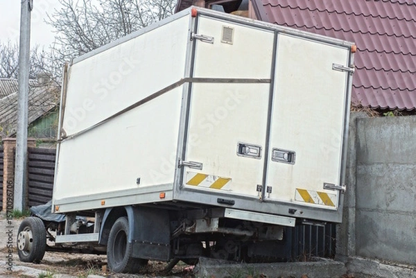 Fototapeta one large closed white trailer on wheels stands on a city street by the road
