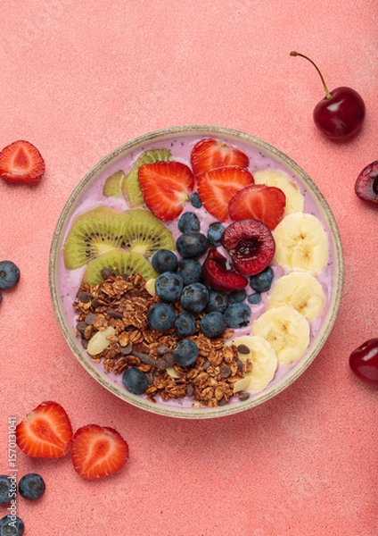 Obraz Vibrant and nutritious acai bowl topped with sliced kiwi, strawberries, blueberries, cherries, banana, and granola, a colorful and healthy meal or breakfast on a pink background