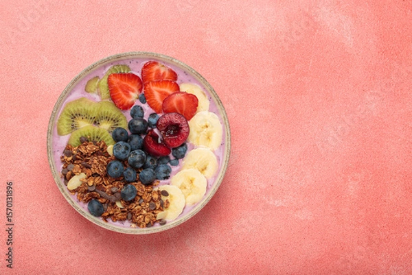 Obraz Vibrant and nutritious acai bowl topped with sliced kiwi, strawberries, blueberries, cherries, banana, and granola, a colorful and healthy meal or breakfast on a pink background, copy space