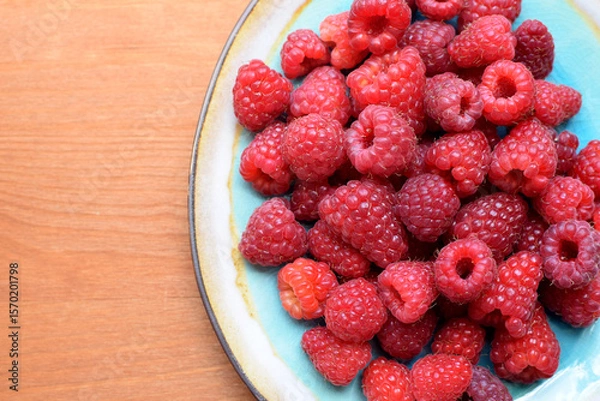 Fototapeta Ripe red raspberries on a blue plate on a wooden background. Sweet raspberry background. Berries close-up. Healthy food.
