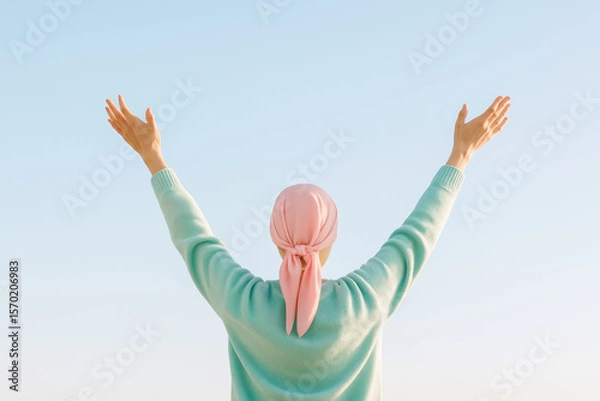 Fototapeta Woman with headscarf raising her arms to a clear, bright sky with a soft gradient evoking hope and positivity