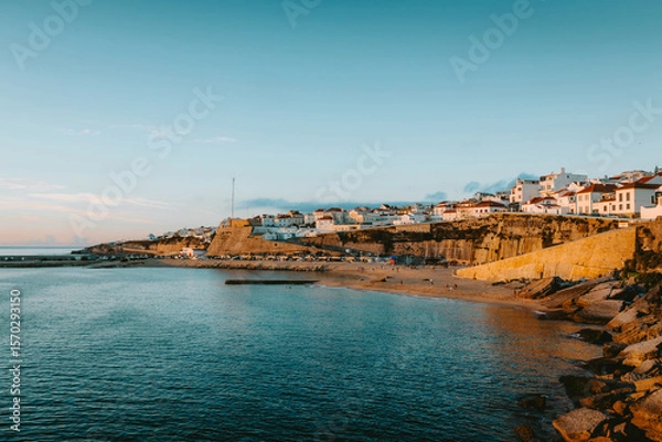Obraz Golden hour sunlight illuminating the picturesque village of Ericeira atop cliffs overlooking the sandy beach and calm Atlantic waters in Mafra, Lisbon, Portugal