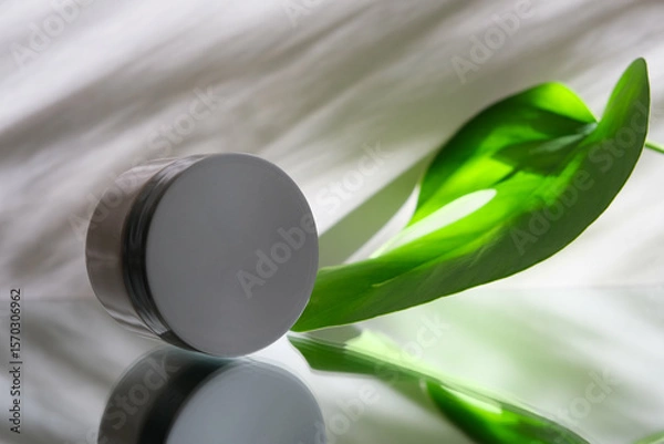 Fototapeta White jar with skincare product. Mirror reflection wet surface. Tropical nature. Wellness, mockup and beauty concept. Package