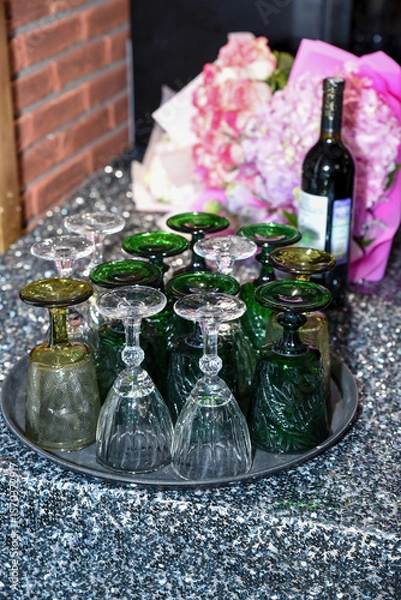Fototapeta Colorful vintage wine glasses upside down on a tray with flowers and wine bottle nearby. Festive table setting ready for a celebration or elegant party.
