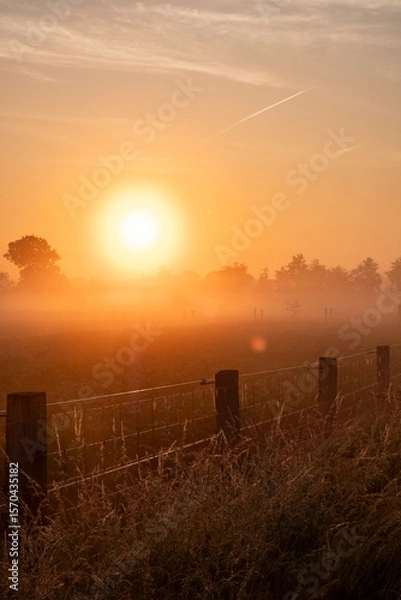 Fototapeta A beautiful and tranquil sunrise gently illuminating a misty countryside landscape adorned with a rustic fence