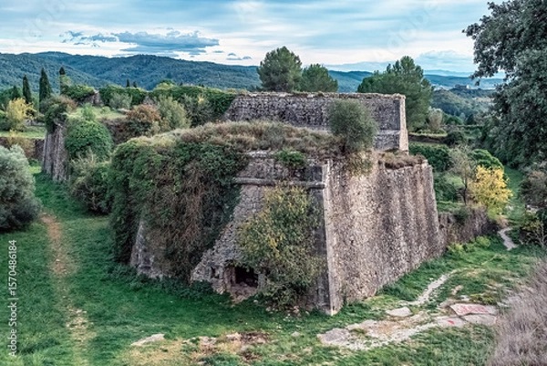 Fototapeta Ancient 17th-century Montjuïc Castle bastion in Girona, Spain, with angled stone walls amid greenery. Historic fortification stands against rolling mountains and blue sky, blending nature and history