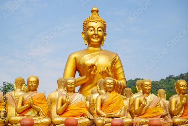 Fototapeta The big golden Buddha statue among many small Buddha statues in countryside public temple named MAKHA BUCHA BUDDHIST MEMORIAL PARK, select and soft focus.