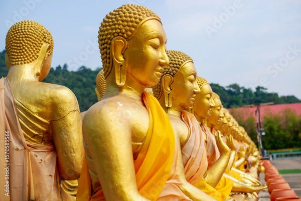 Fototapeta The big golden Buddha statue among many small Buddha statues in countryside public temple named MAKHA BUCHA BUDDHIST MEMORIAL PARK, select and soft focus.