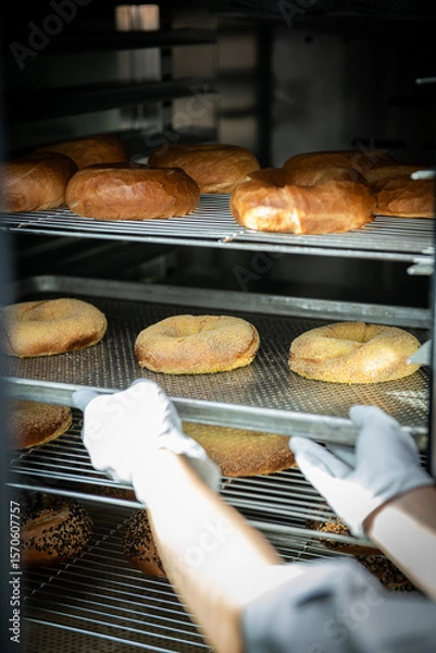 Fototapeta Baker putting fresh bagels in the oven at the bakery.