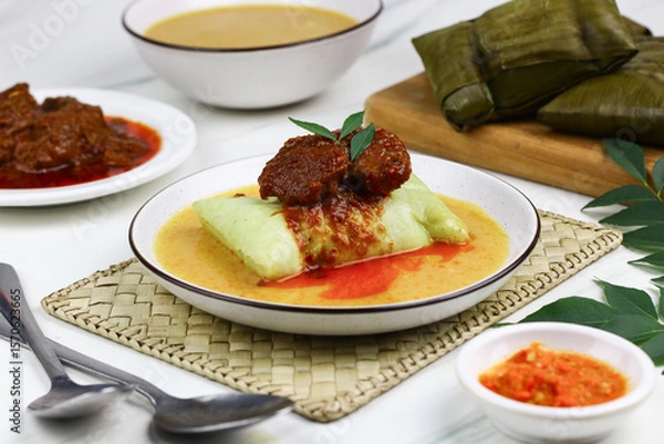 Fototapeta Buras, Indonesian traditional rice cakes from Makassar, South Sulawesi. Buras made from rice, coconut milk and salt wrapped with banana leaves and served with savory soup and beef or chicken.