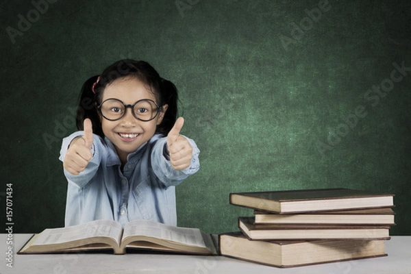 Fototapeta Primary student with ok gesture and books on table