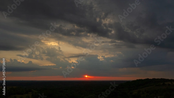 Fototapeta Evening rain clouds in the sky and sun on the horizon line at sunset.
