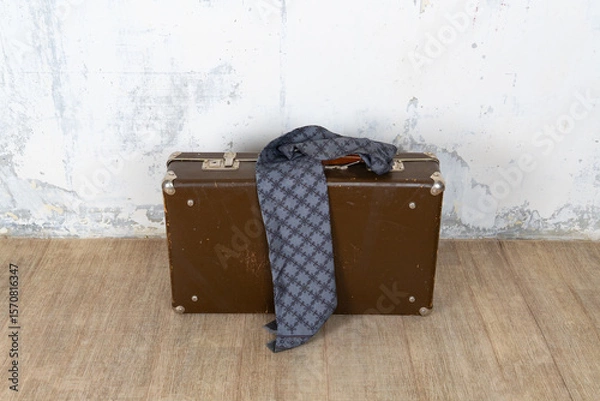 Fototapeta Vintage retro suitcase, the suitcase and there is a scarf on it, stand on a stool. The background is a white wall. The concept of retro travel and retro design.
