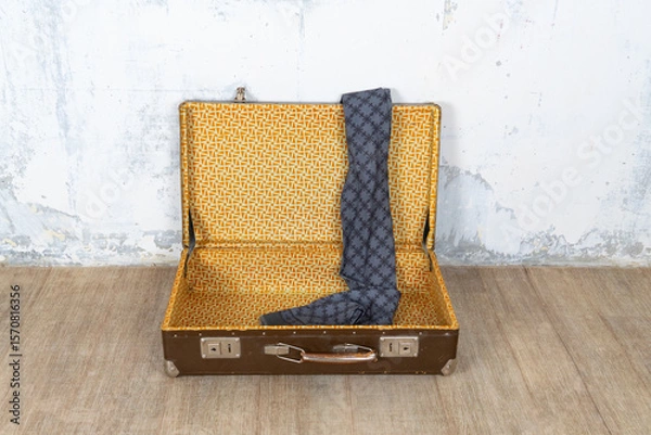 Fototapeta Vintage retro suitcase, the suitcase is open and there is a scarf in it, stand on a stool. The background is a white wall. The concept of retro travel and retro design.