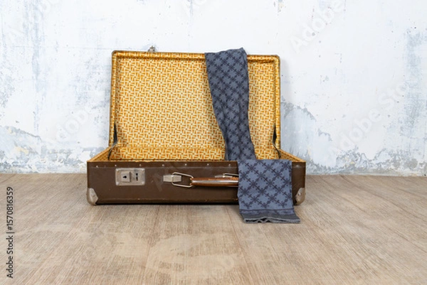 Fototapeta Vintage retro suitcase, the suitcase is open and there is a scarf in it, stand on a stool. The background is a white wall. The concept of retro travel and retro design.