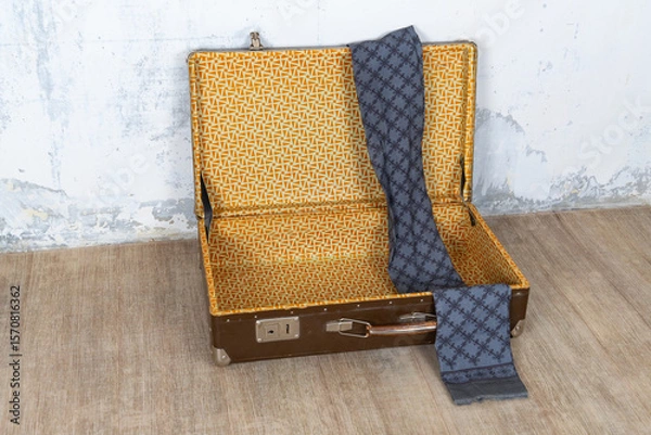 Fototapeta Vintage retro suitcase, the suitcase is open and there is a scarf in it, stand on a stool. The background is a white wall. The concept of retro travel and retro design.