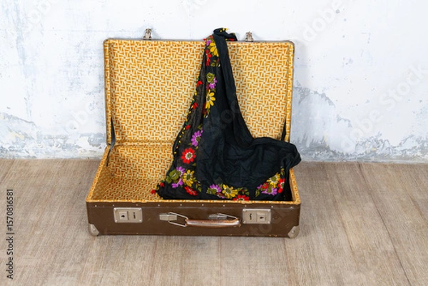 Fototapeta Vintage retro suitcase, the suitcase is open and there is a scarf in it, stand on a stool. The background is a white wall. The concept of retro travel and retro design.