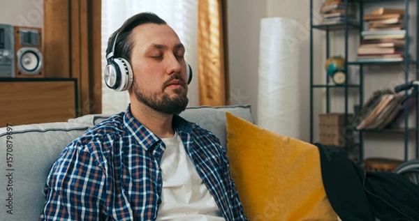 Fototapeta A middle-aged man enjoys an afternoon at home with music in his headphones, pausing as a friend sends a message about a friendly get-together, bringing a smile to his face.