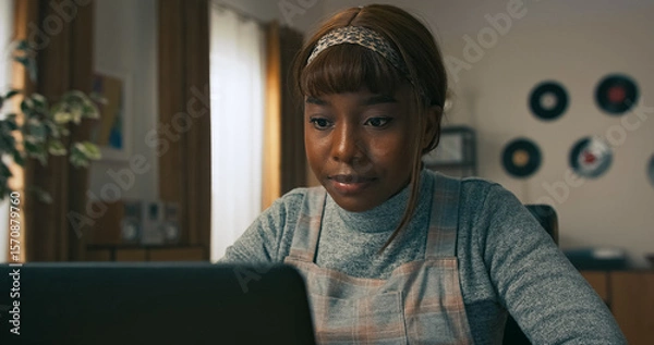 Fototapeta A pretty young girl sits at a home office desk, looking over her calendar and jotting down plans for the week ahead, focused on staying productive and balanced in her work routine.