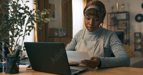 Fototapeta Focused on staying efficient, a young girl uses her work break to reply to delayed messages. She takes notes at her desk to avoid forgetting anything important.