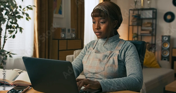 Fototapeta A professional woman is seated at her workstation, actively working on a laptop. She remains focused as she handles important projects, symbolizing work in progress and commitment.