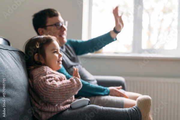Fototapeta Happy father with child playing wireless console game station. Funny weekend family time at home in living room.