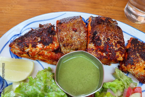 Fototapeta Tandoori trout fish grilled to perfection, served with tangy green chutney, lemon wedge, and fresh green salad. A flavorful Indian dish ideal for seafood lovers. Great for healthy meals.