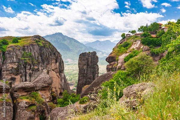 Fototapeta View of dramatic Meteora rock formations and distant village from grassy cliffside in Meteora Greece