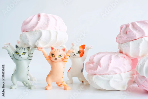 Obraz Funny toy kittens lift a pink-and-white marshmallow treat together in a playful delivery concept on a clean white background. Photo